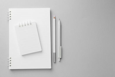Photo of White notebooks, pen and pencil on light grey background, top view. Space for text