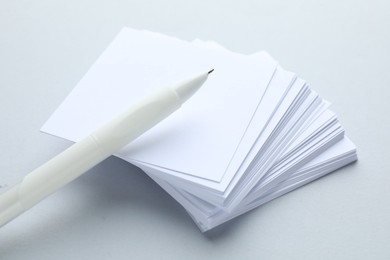 Photo of White pen and note papers on light grey background, closeup