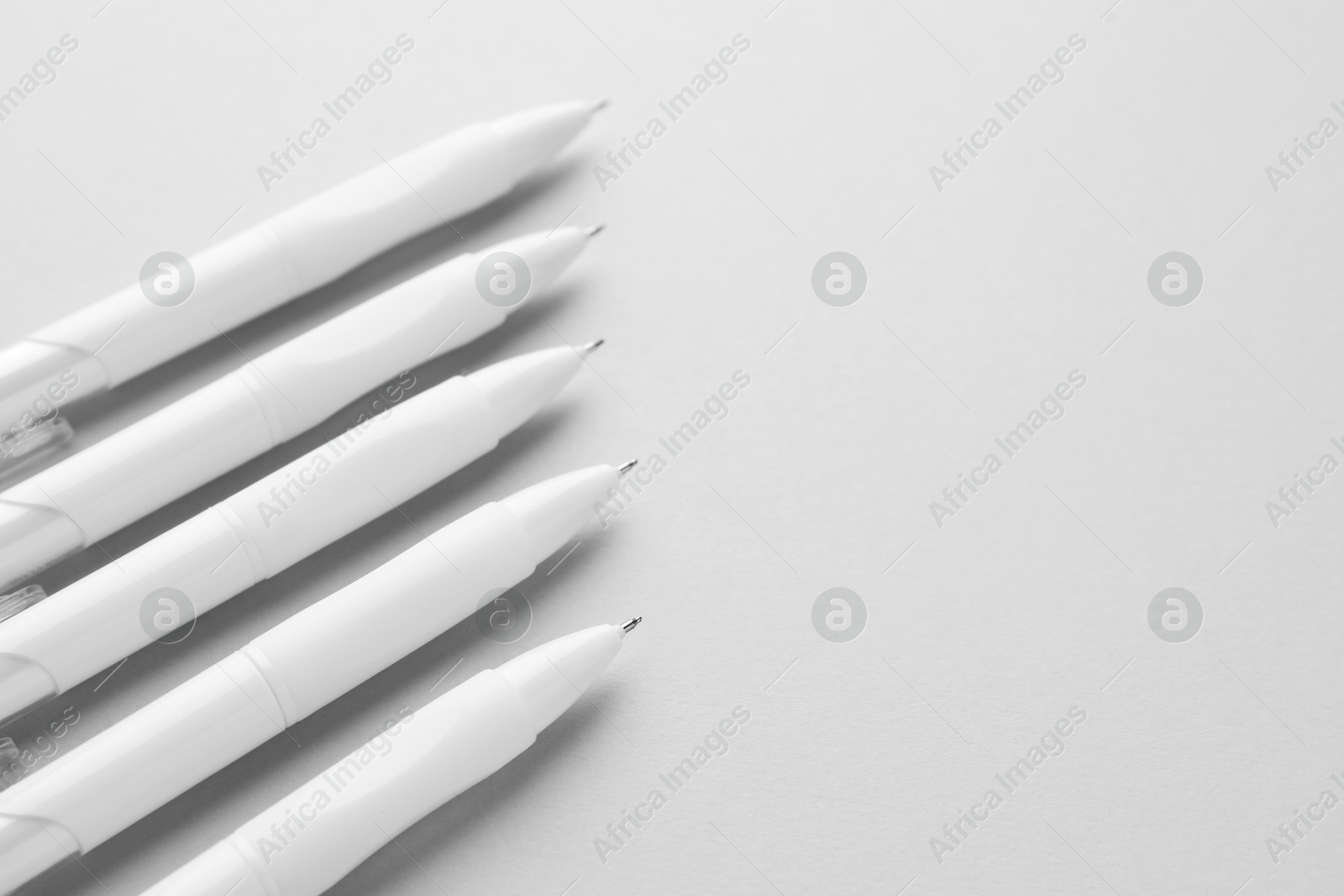 Photo of White pens on light grey background, closeup. Space for text