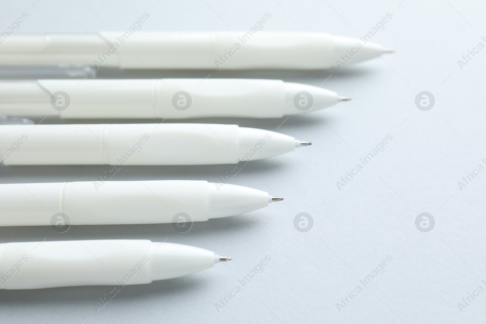 Photo of White pens on light grey background, closeup. Space for text