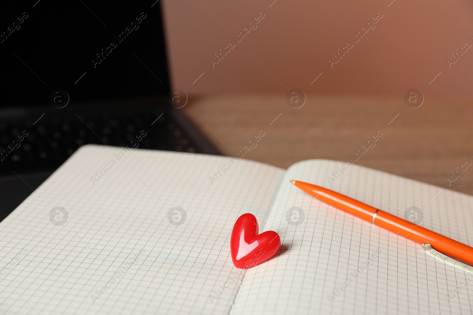 Photo of Online dating site. Notebook with red heart, pen and laptop on table, closeup