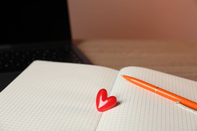 Photo of Online dating site. Notebook with red heart, pen and laptop on table, closeup