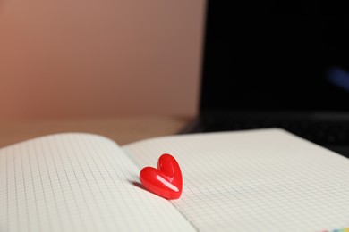 Photo of Online dating site. Notebook with red heart and laptop on table, closeup