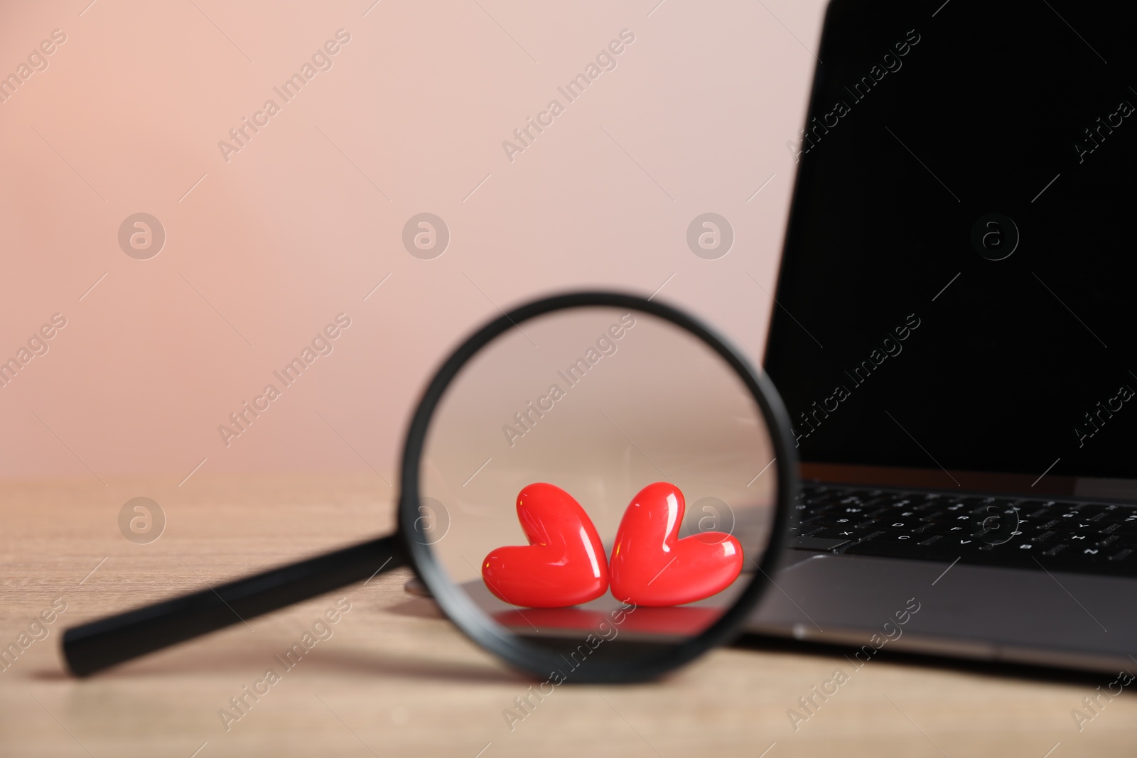 Online dating site. Laptop, red hearts and magnifying glass on wooden table, closeup Photo of Online dating site. Laptop, red hearts and magnifying glass on wooden table, closeup