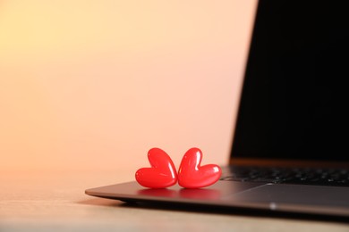 Photo of Online dating site. Laptop and red hearts on table, closeup