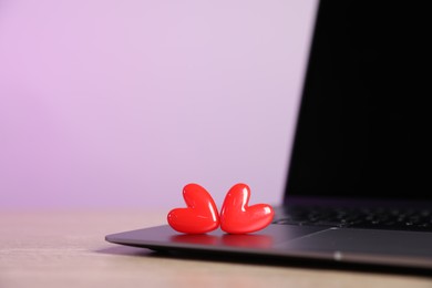 Photo of Online dating site. Laptop and red hearts on table, closeup