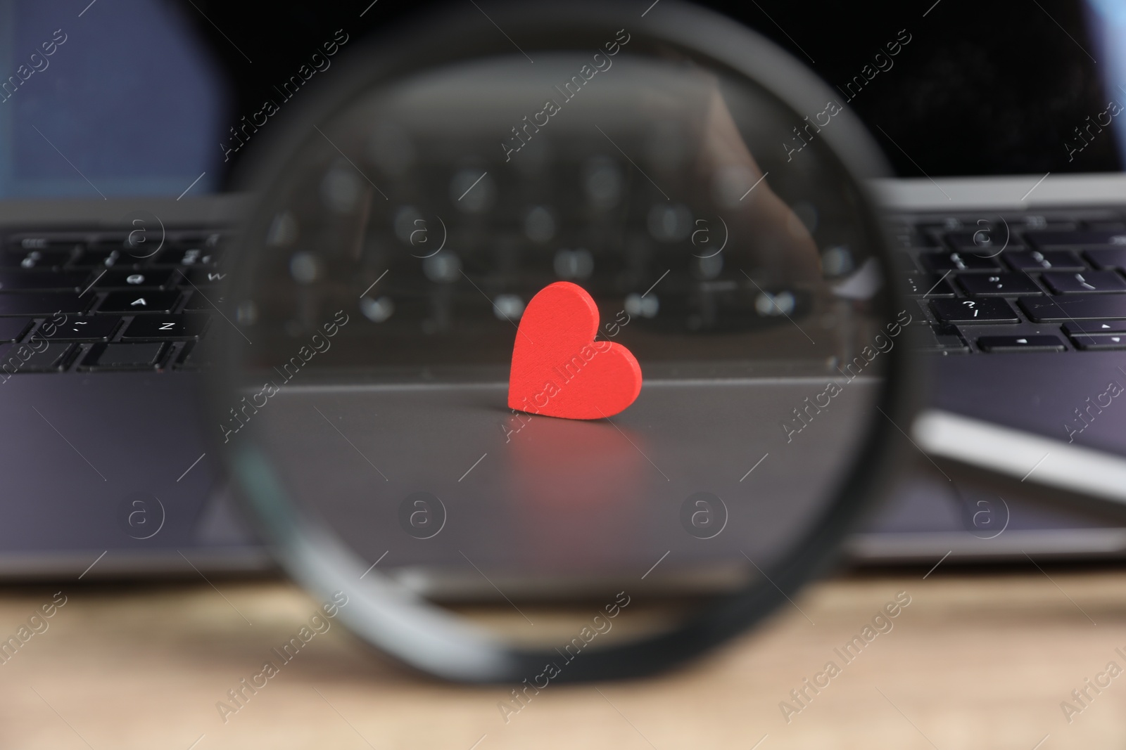 Online dating site. Laptop, red heart and magnifying glass on table, closeup Photo of Online dating site. Laptop, red heart and magnifying glass on table, closeup
