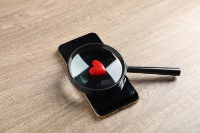 Photo of Online dating site. Smartphone, red heart and magnifying glass on wooden table, above view