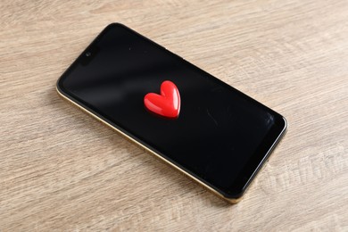 Photo of Online dating site. Smartphone and red heart on wooden table, above view