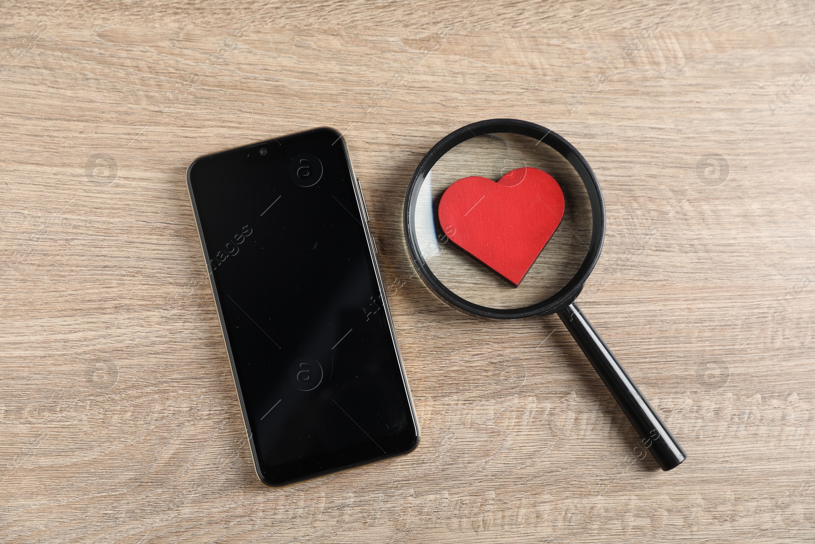 Online dating site. Smartphone, red heart and magnifying glass on wooden table, flat lay Photo of Online dating site. Smartphone, red heart and magnifying glass on wooden table, flat lay