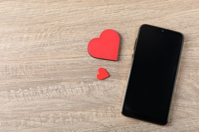 Photo of Online dating site. Smartphone and red hearts on wooden table, flat lay. Space for text