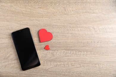 Photo of Online dating site. Smartphone and red hearts on wooden table, flat lay. Space for text