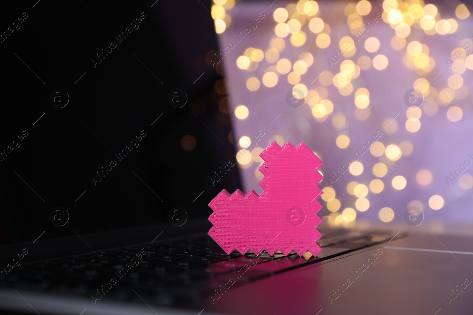 Online dating site. Pink heart on laptop against blurred lights, closeup. Bokeh effect Photo of Online dating site. Pink heart on laptop against blurred lights, closeup. Bokeh effect