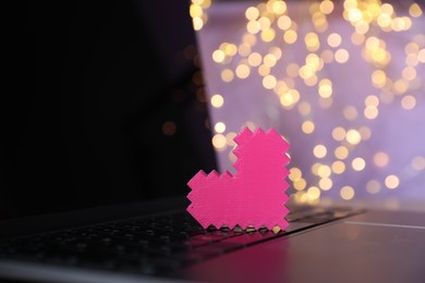 Photo of Online dating site. Pink heart on laptop against blurred lights, closeup. Bokeh effect