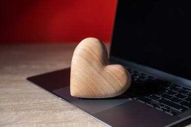 Photo of Online dating site. Wooden heart and laptop on table, closeup