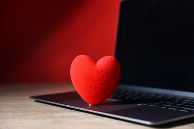 Photo of Online dating site. Red heart and laptop on wooden table, closeup