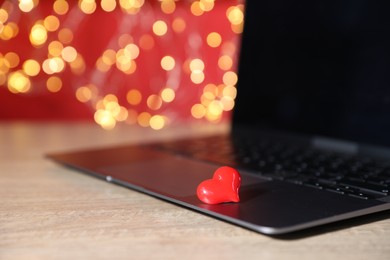 Photo of Online dating site. Red heart and laptop on wooden table against blurred lights, closeup. Bokeh effect