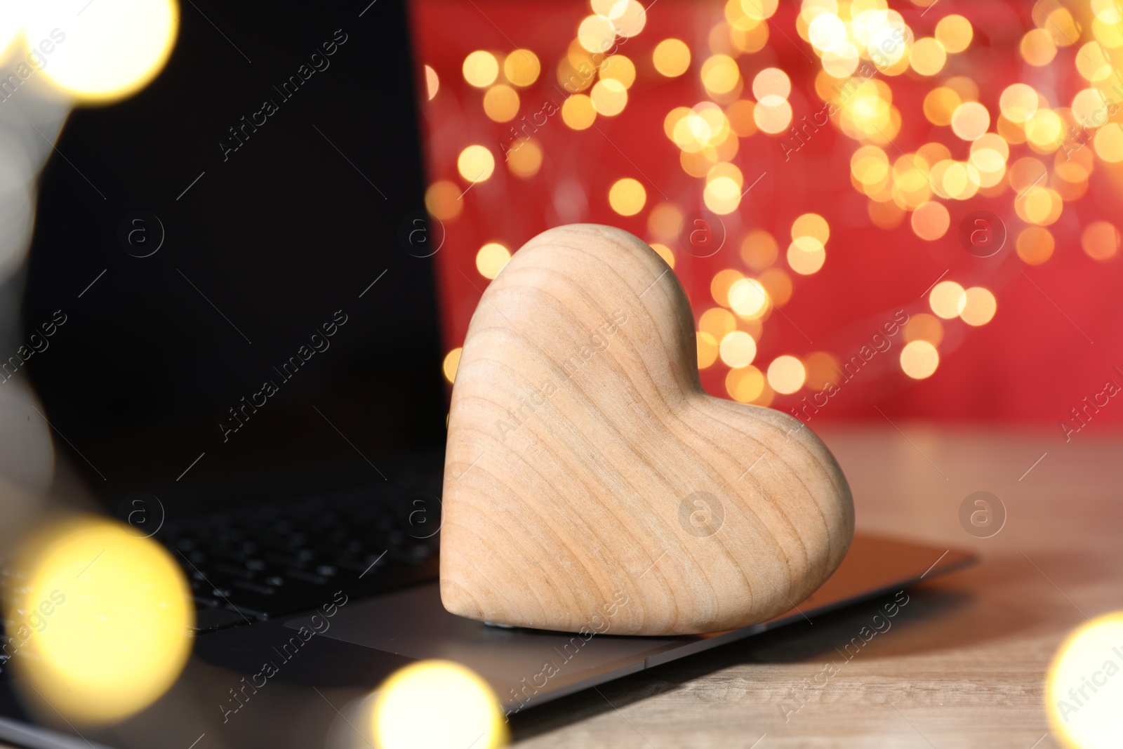 Online dating site. Wooden heart and laptop on table against blurred lights, closeup. Bokeh effect Photo of Online dating site. Wooden heart and laptop on table against blurred lights, closeup. Bokeh effect