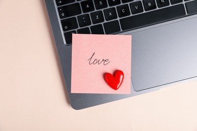 Photo of Online dating site. Sticky note with word Love, red heart and laptop on beige background, top view