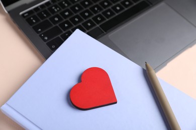 Photo of Online dating site. Laptop, notebook, red heart and pen on beige background, closeup
