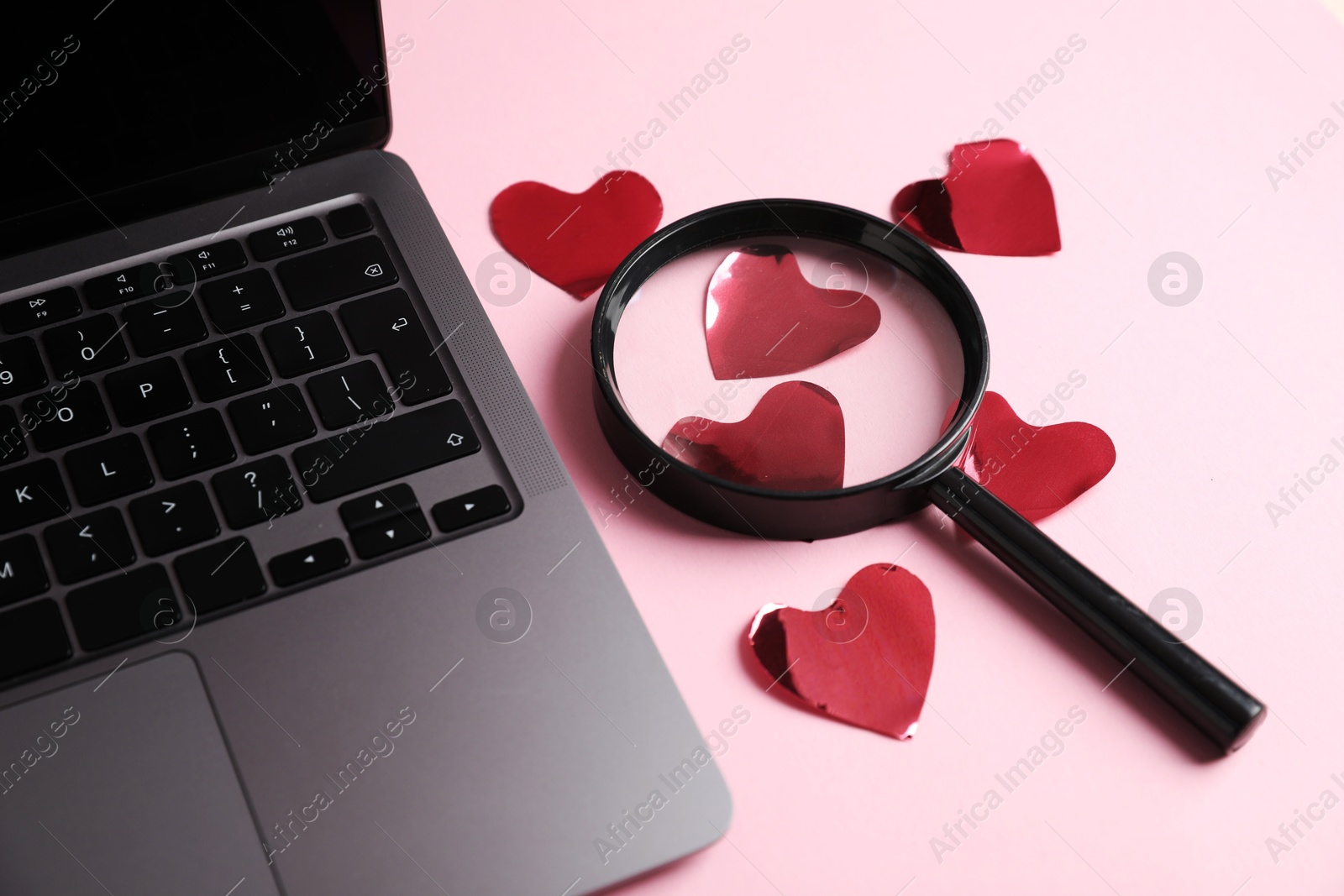 Photo of Online dating site. Many red hearts, magnifying glass and laptop on pink background, closeup