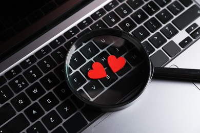 Photo of Online dating site. Red hearts and magnifying glass on laptop, above view