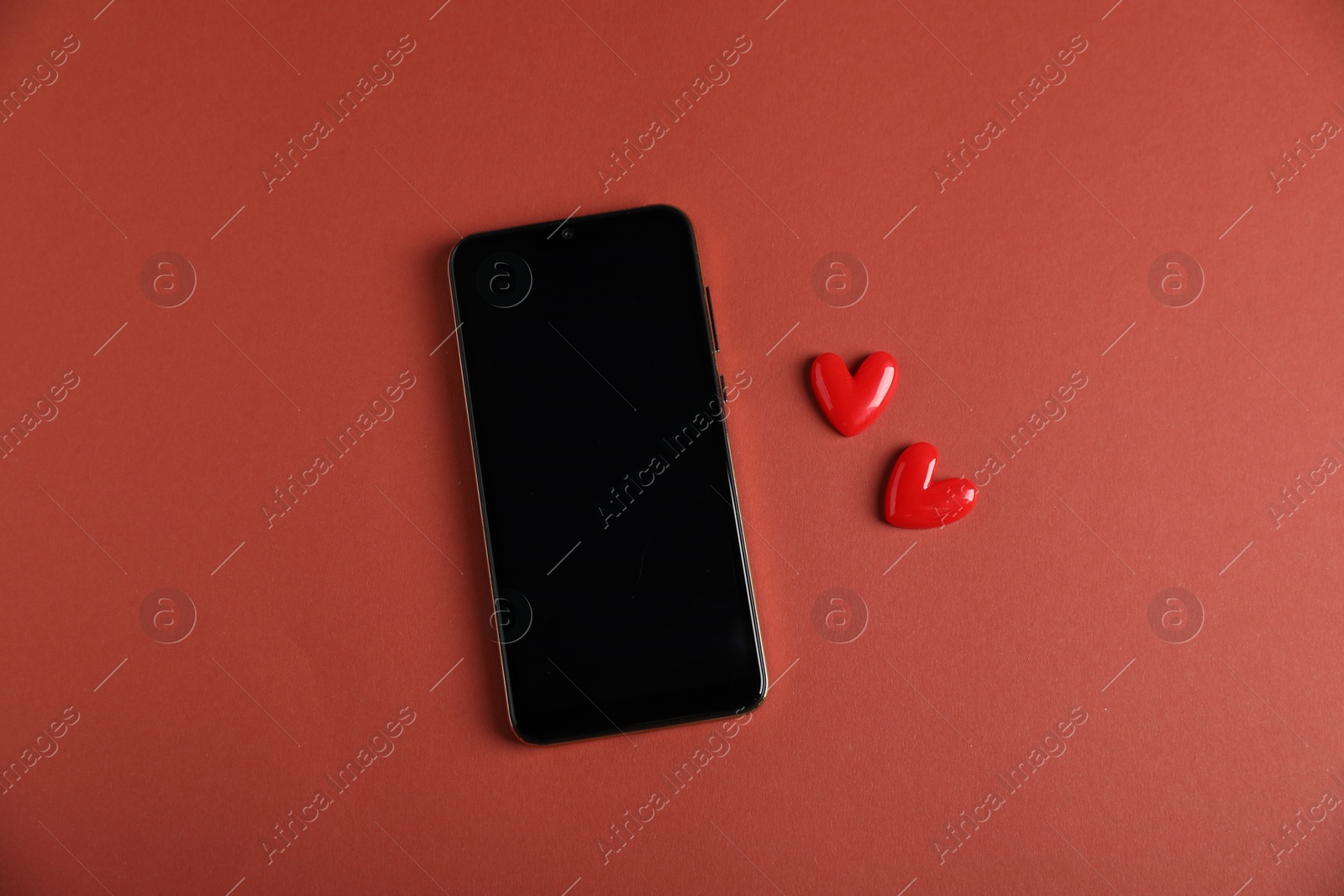 Photo of Online dating site. Smartphone and hearts on red-brown background, flat lay