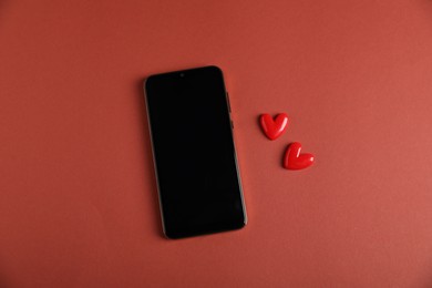 Photo of Online dating site. Smartphone and hearts on red-brown background, flat lay