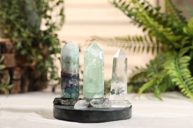 Photo of Aura. Beautiful crystals on beige fabric and green plants indoors