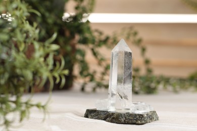 Photo of Aura. Beautiful crystal on beige fabric and green plants indoors