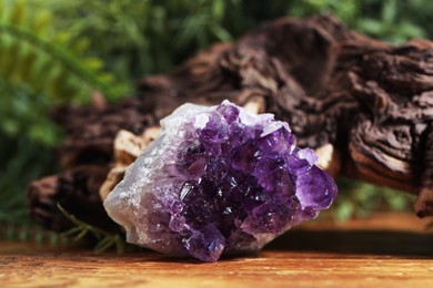 Photo of Aura. Beautiful amethyst and driftwood on wooden surface against blurred green background