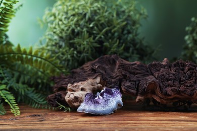 Photo of Aura. Beautiful amethyst, driftwood and green plants on wooden surface against blurred background