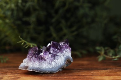 Photo of Aura. Beautiful amethyst on wooden surface against blurred green background, closeup