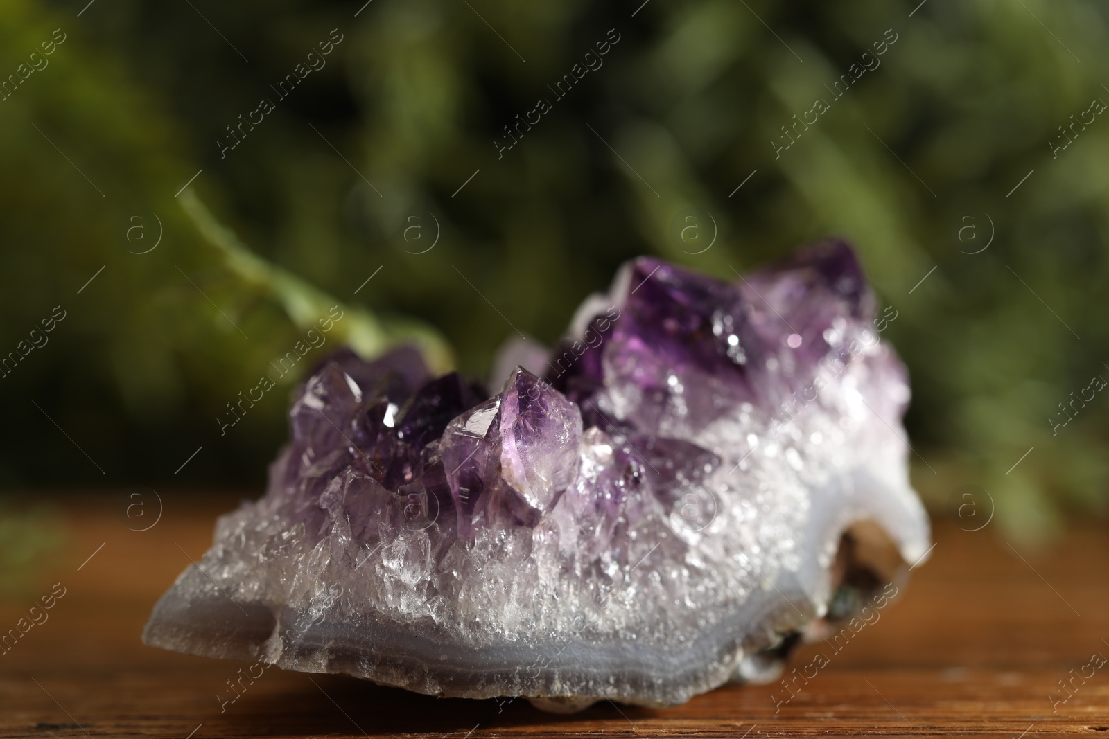 Photo of Aura. Beautiful amethyst on wooden surface against blurred green background, closeup