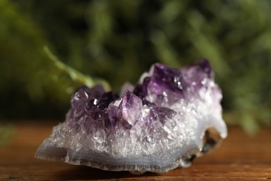 Photo of Aura. Beautiful amethyst on wooden surface against blurred green background, closeup