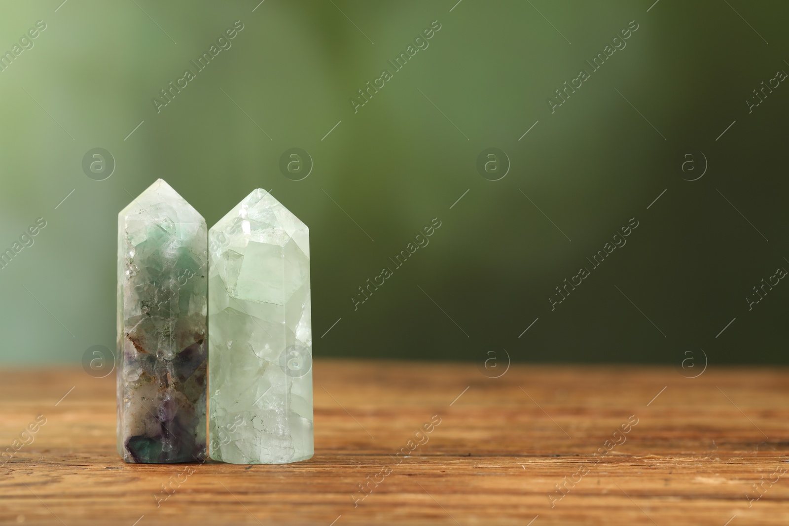Photo of Aura. Beautiful crystals on wooden surface against blurred green background. Space for text