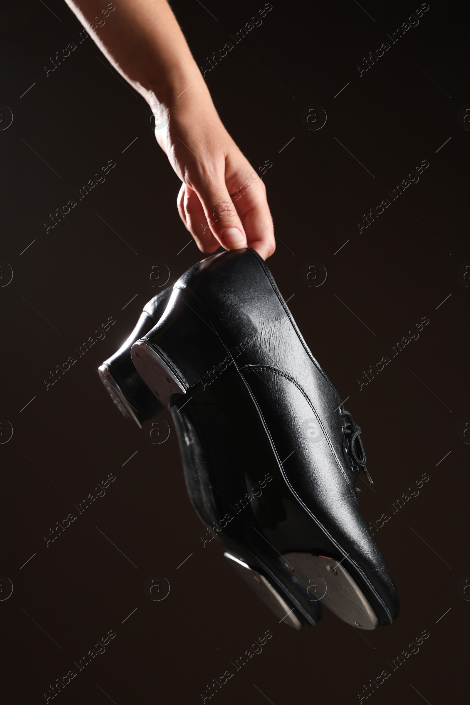 Photo of Woman holding tap shoes on dark background, closeup. Tap dance