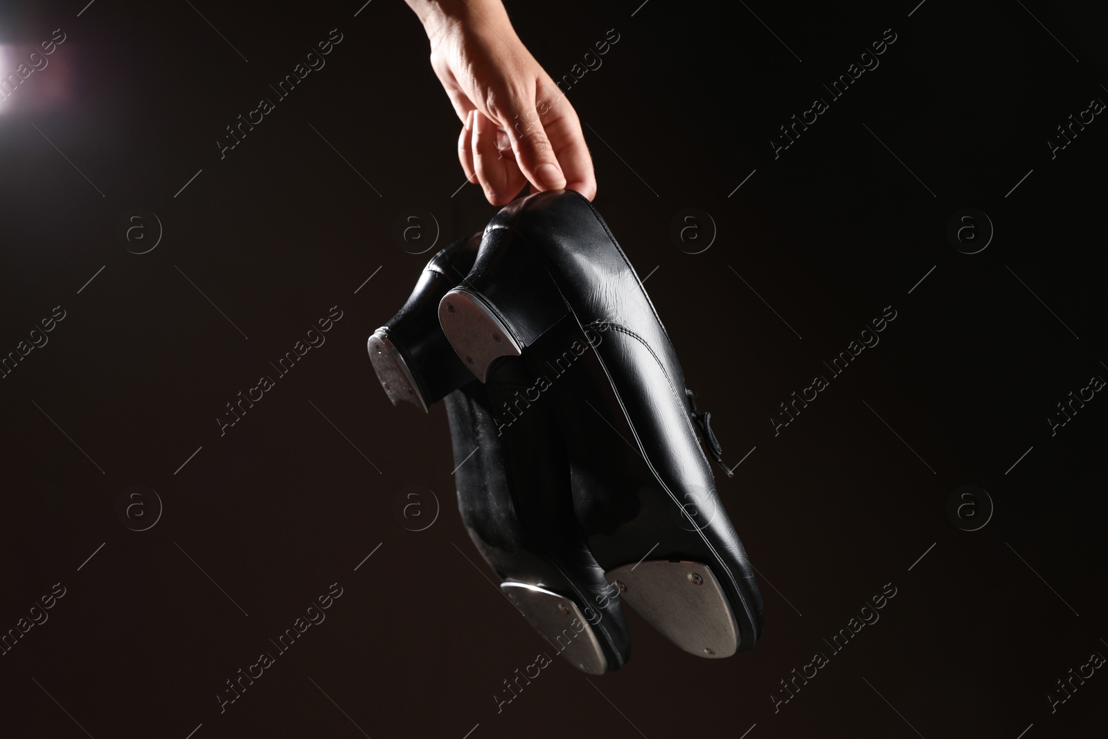 Photo of Woman holding tap shoes on dark background, closeup. Tap dance