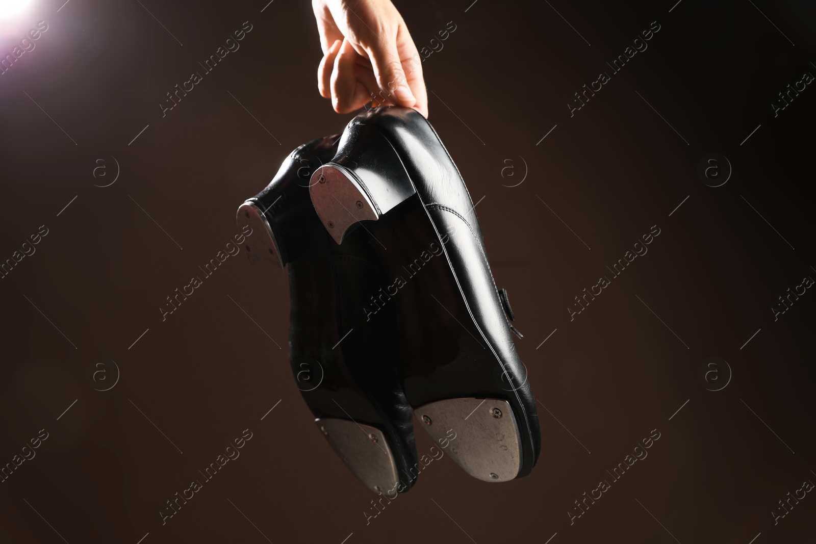 Photo of Woman holding tap shoes on dark background, closeup. Tap dance