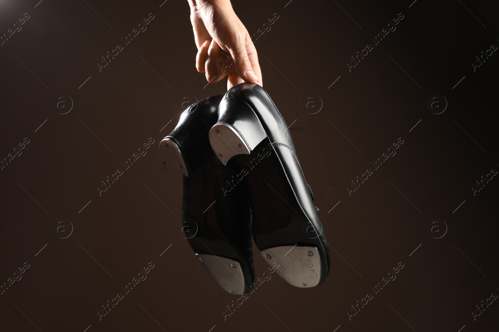 Photo of Woman holding tap shoes on dark background, closeup. Tap dance
