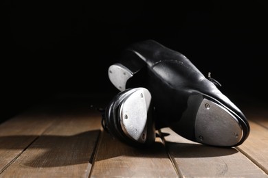 Photo of Pair of tap shoes on wooden floor against black background, closeup. Tap dance