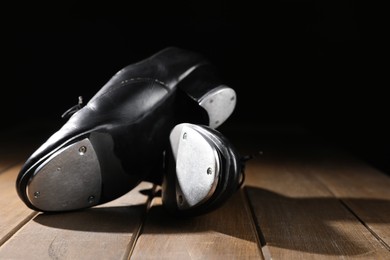 Photo of Pair of tap shoes on wooden floor against black background, closeup. Tap dance