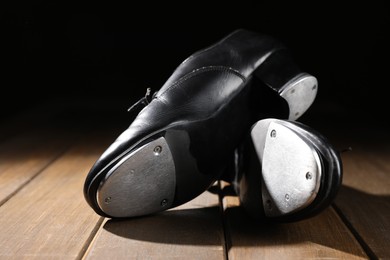 Photo of Pair of tap shoes on wooden floor against black background, closeup. Tap dance