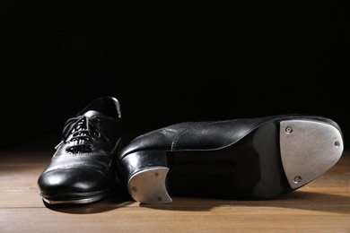 Photo of Pair of tap shoes on wooden floor against black background, closeup. Tap dance
