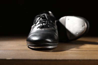 Photo of Pair of tap shoes on wooden floor against black background, closeup. Tap dance