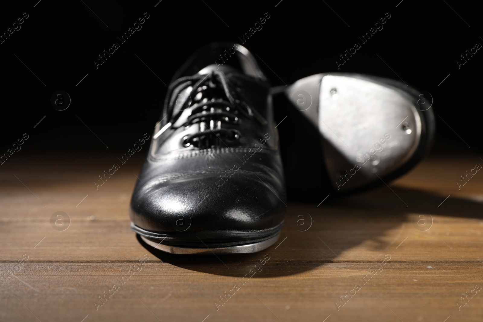 Pair of tap shoes on wooden floor against black background, closeup. Tap dance Photo of Pair of tap shoes on wooden floor against black background, closeup. Tap dance