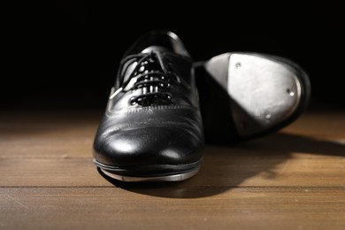 Photo of Pair of tap shoes on wooden floor against black background, closeup. Tap dance