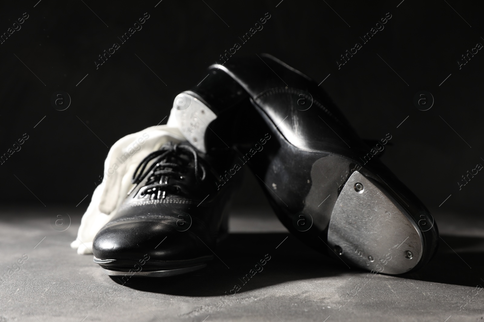Photo of Pair of shoes for tap dance and white gloves on grey surface against black background, closeup