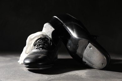 Photo of Pair of shoes for tap dance and white gloves on grey surface against black background, closeup