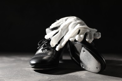 Photo of Pair of shoes for tap dance and white gloves on grey surface against black background, closeup